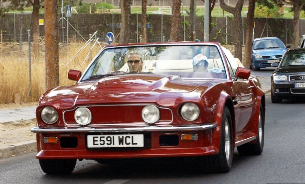 David and Victoria Beckham cruise in their red Aston Martin V8 Volante